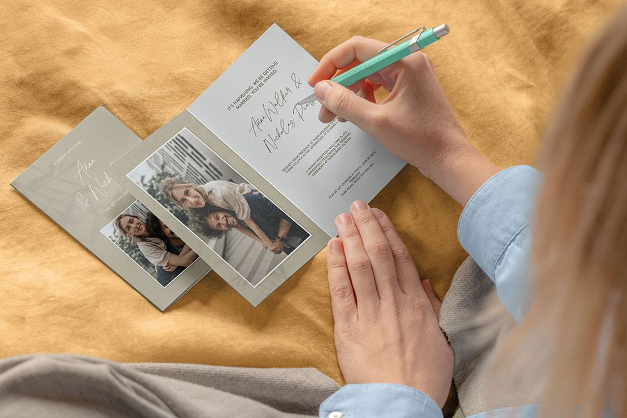 Una mano sostiene un bolígrafo lista para escribir en una invitación de boda personalizada, como inspiración para los detalles de una checklist de fotos antes de la ceremonia de boda.