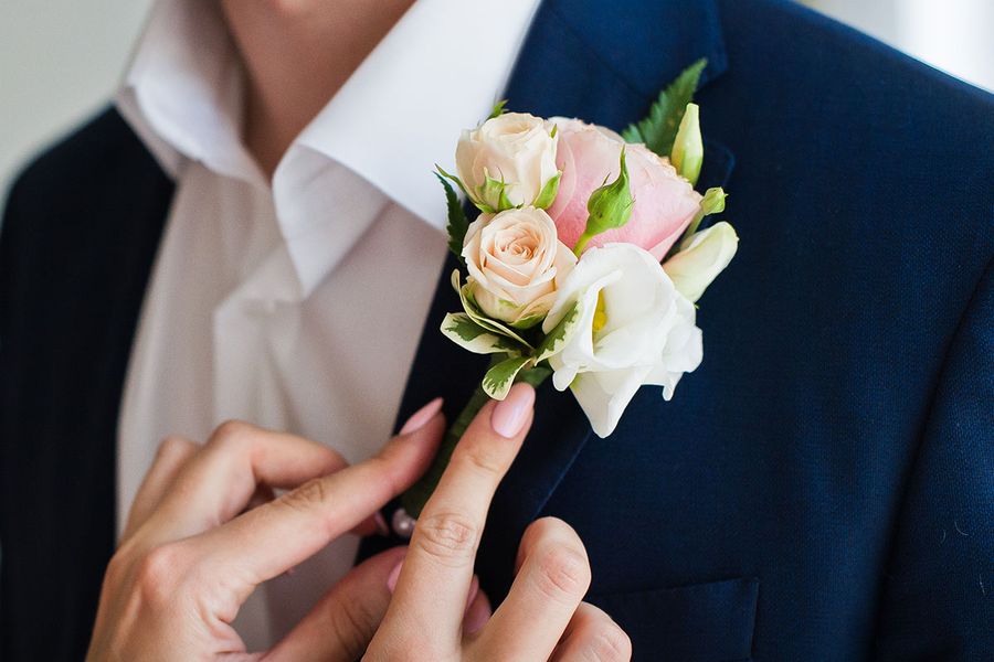 Primer plano de alguien colocando un boutonnière en el ojal del traje del novio, capturando un detalle de la checklist de fotos del novio preparándose.
