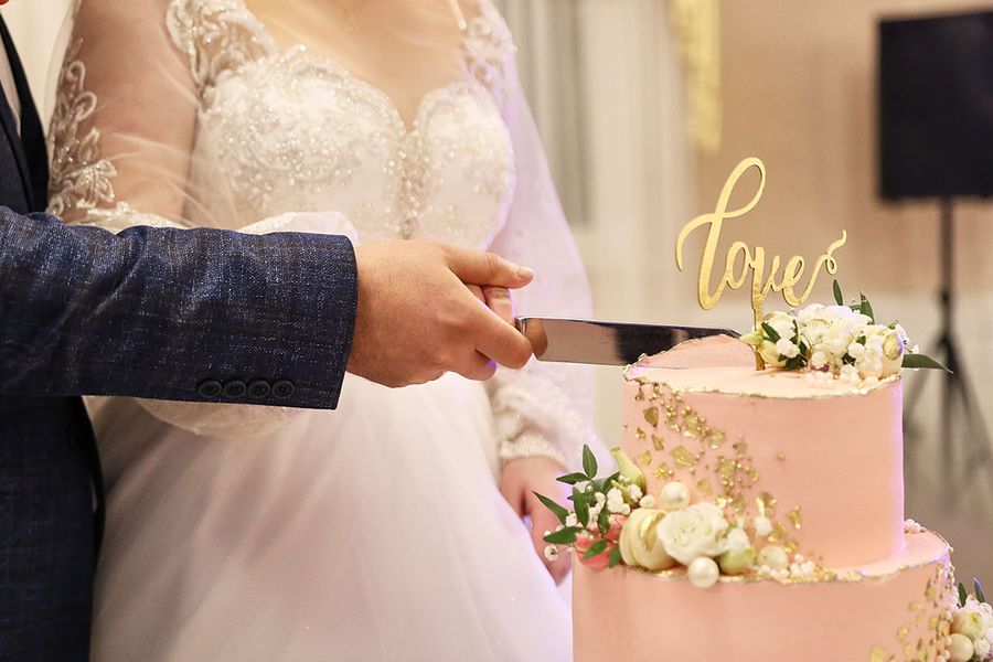 Primer plano de las manos de la novia y el novio mientras cortan su tarta de boda, capturando un detalle clásico de la checklist de fotos de comida en la boda.