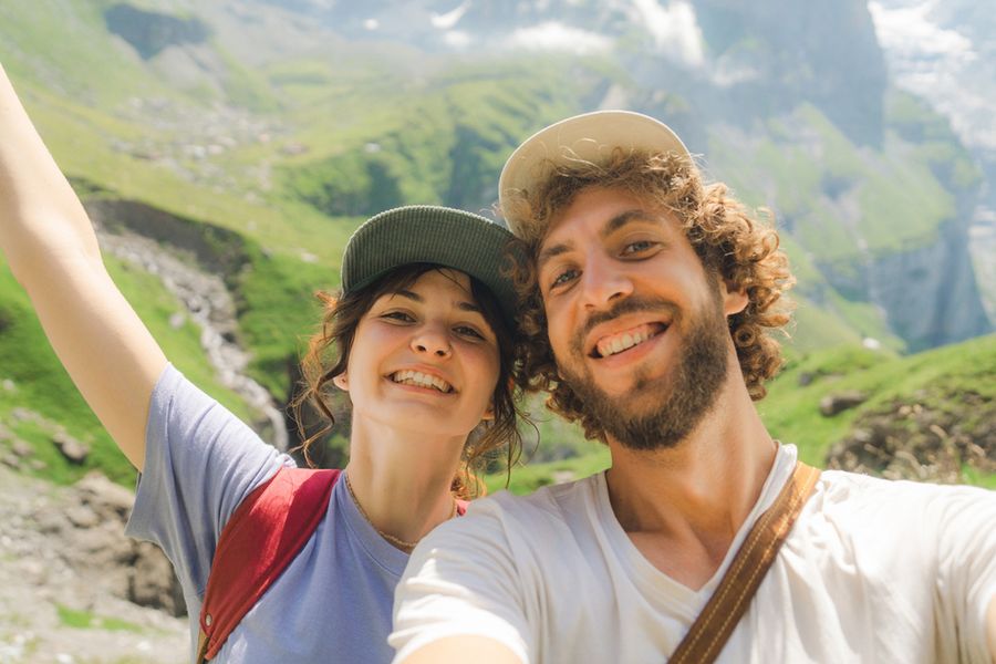 Una pareja sonriente en un paisaje montañoso durante una aventura de verano, perfecta para elegir frases para fotos de verano en Instagram o en un álbum de fotos de Hofmann.