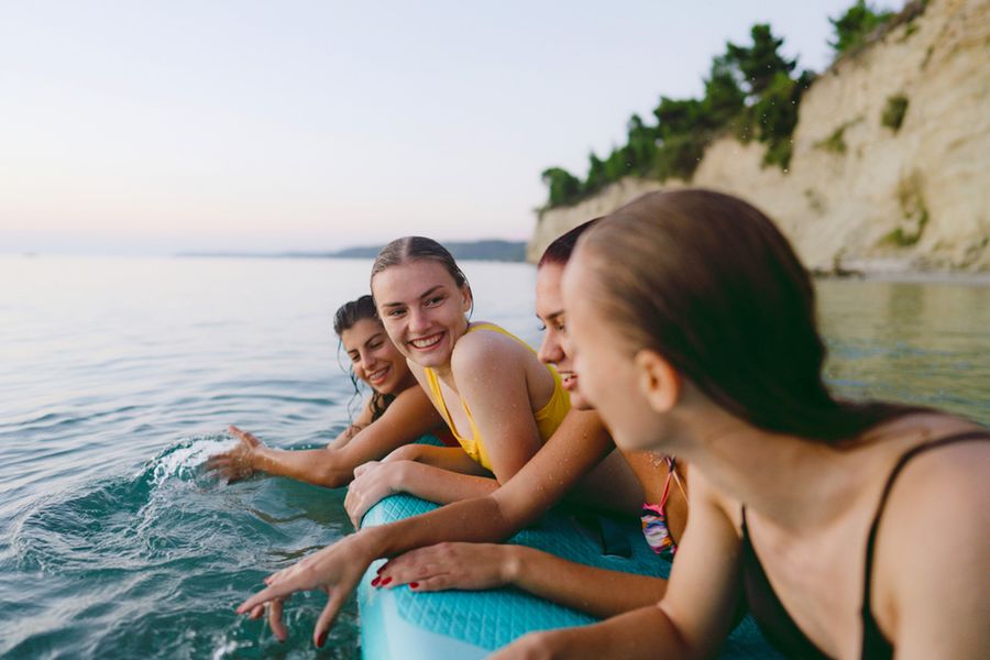 Cuatro amigas en el mar descansando sobre un flotador en vacaciones de verano, perfecto para buscar frases de verano para Instagram o álbumes de Hofmann.