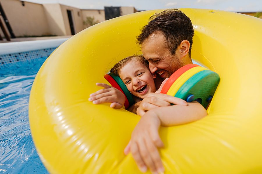 Un padre y su hijo en un flotador en una piscina durante las vacaciones, perfecto para buscar frases para fotos de verano en redes sociales con Hofmann.