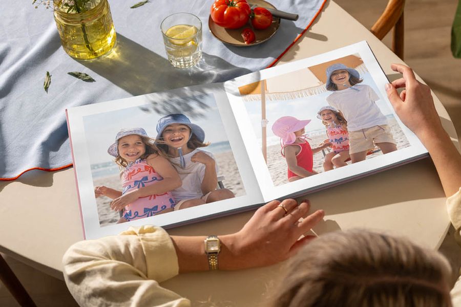 Un fotolibro abierto sobre una mesa de cocina muestra imágenes de niñas divirtiéndose en la playa, ilustrando el consejo de Hofmann para recordar los momentos del verano con un fotolibro personalizado.