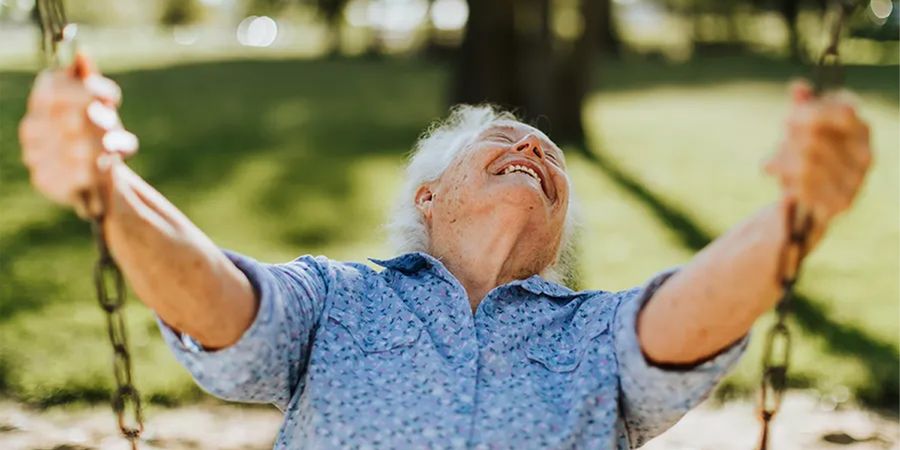 Un hombre mayor sonriendo en un columpio al aire libre en un bonito día de primavera, como inspiración para Hofmann y para capturar fotos de primavera llenas de sol y color.