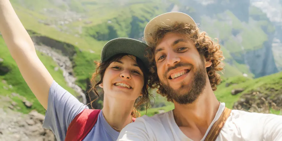 Una pareja sonriente en un paisaje montañoso durante una aventura de verano, perfecta para elegir frases para fotos de verano en Instagram o en un álbum de fotos de Hofmann.