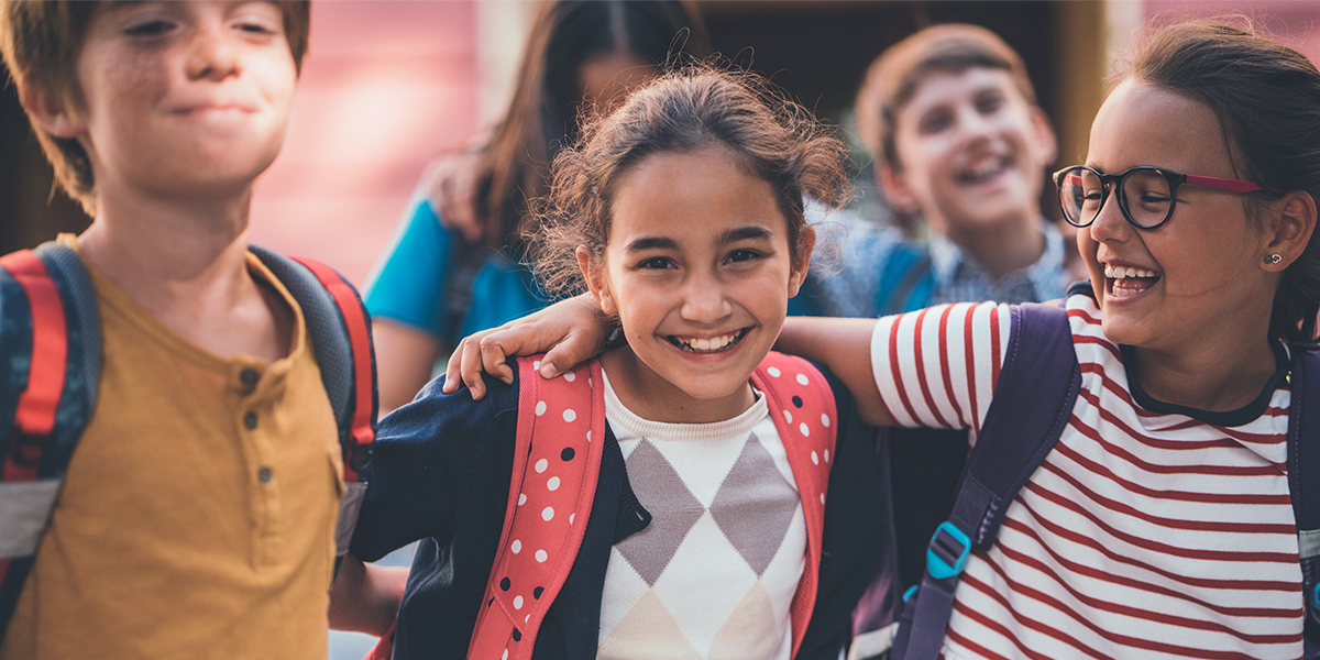 Tres amigos del colegio se abrazan y sonríen a la cámara, capturando la alegría del primer día de cole en la guía de Hofmann para hacer fotos increíbles del primer día de colegio.