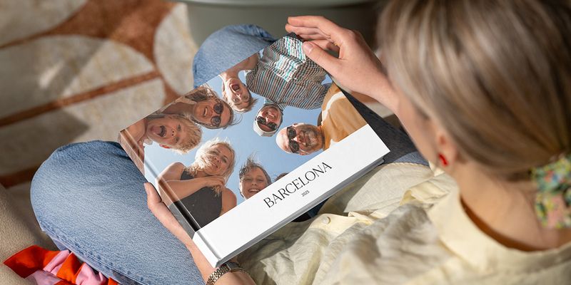 Una mujer mira un álbum de fotos titulado 'Barcelona', con una imagen de muchos rostros sonrientes de la familia mirando hacia la cámara, ilustrando la guía de Hofmann para crear un álbum de fotos de vacaciones en grupo.