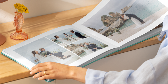Manos de una mujer sujetando abierto un álbum de fotos de boda con una doble página de distintas fotos de una novia y un novio en la playa, para ilustrar las ideas de Hofmann para elegir el título de tu álbum de boda.