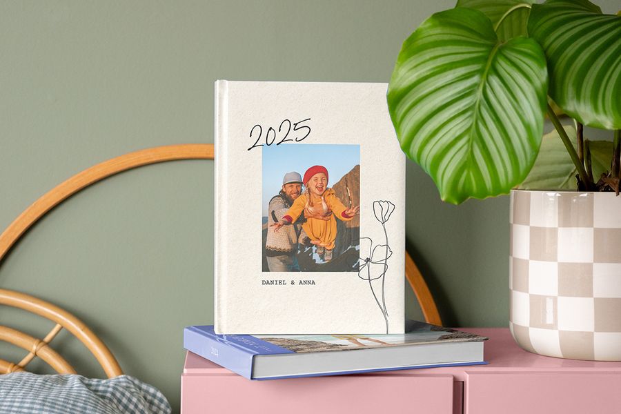 Un álbum anual de 2025 con una imagen de padre e hija en la portada, apoyado sobre el álbum de fotos 2024 en una mesita de noche.