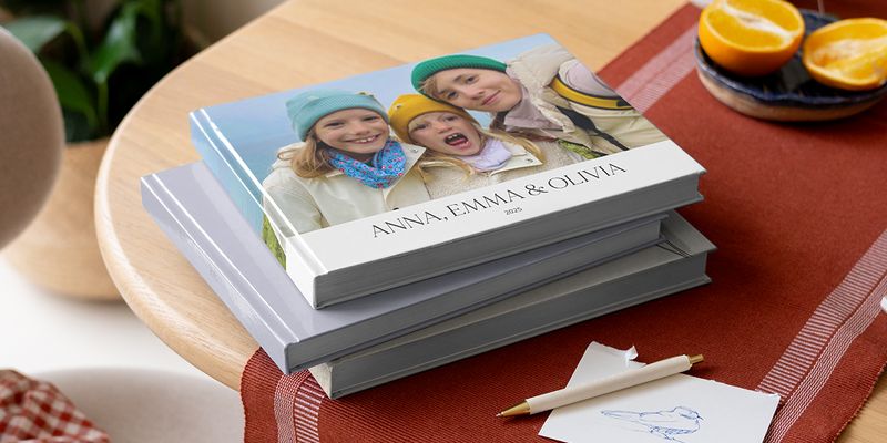 Una selección de álbumes de fotos de Hofmann sobre una mesa con un bolígrafo, con hermanos en la portada para inspirar frases para álbum de fotos familiar.