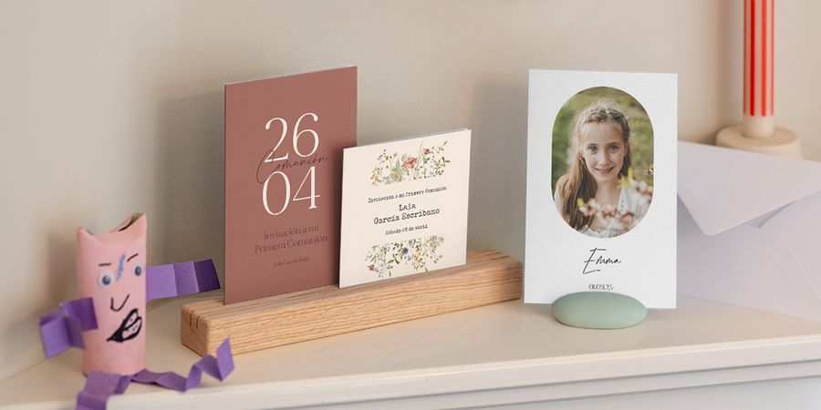 Una gama de diferentes invitaciones de primera comunión de Hofmann mostradas juntas en un estante.