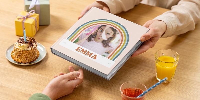 Un album de fotos cumpleaños para Emma se pasa por una mesa con una tarta y un regalo, mostrando cómo crear un album para cumpleaños o un album fotos cumpleaños con Hofmann.