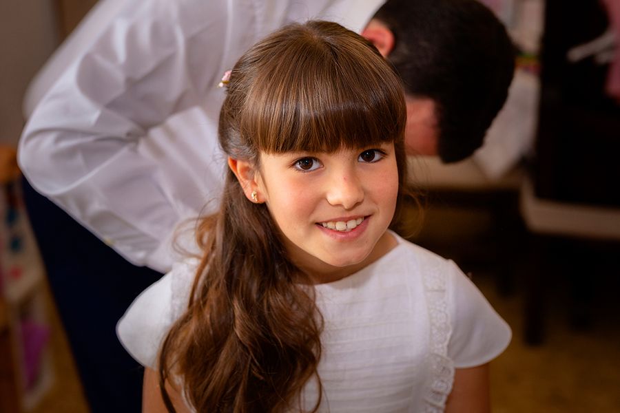 Una niña con un vestido blanco de primera comunion posando con elegancia, como parte de la preparación para una primera comunion inolvidable con Hofmann.