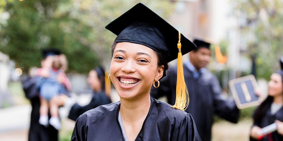 Una graduada sonriente al aire libre con toga y birrete, como inspiración para Hofmann y para ideas de regalos de graduación personalizados.