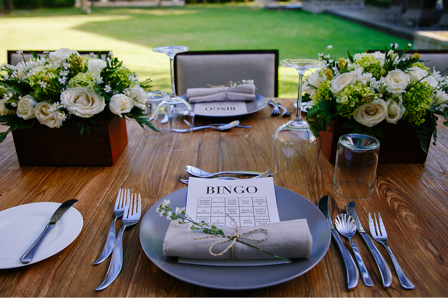 Cartones de bingo de boda colocados sobre una mesa de boda decorada con flores, como inspiración para Hofmann y para juegos de boda y actividades para invitados.