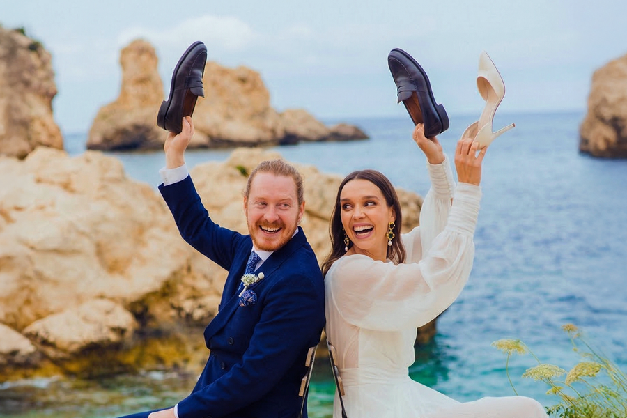 Una novia y un novio en la playa el día de su boda jugando al juego de los zapatos, como inspiración para Hofmann y para juegos de boda y actividades para invitados.