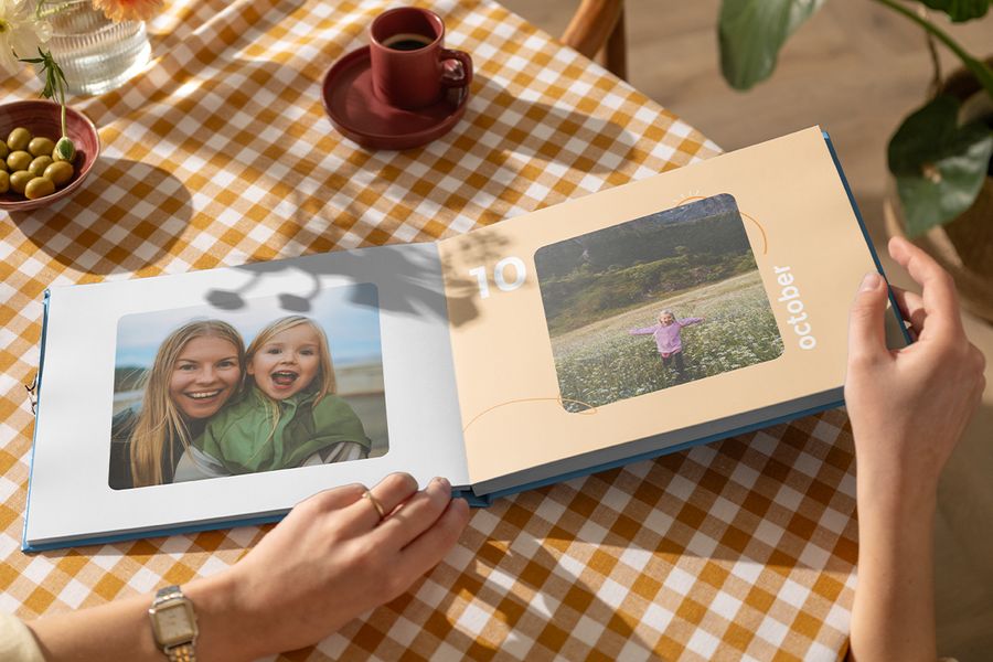 Un coffee table book abierto de Hofmann con una madre y su hija en una página y una niña jugando en un campo de flores en la otra, como inspiración para un coffee table book personalizado y un álbum decorativo familiar.
