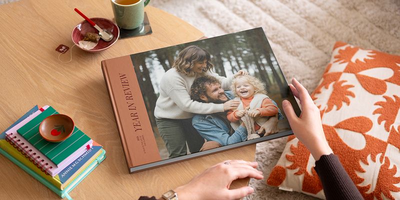 Un álbum decorativo de Hofmann de tipo coffee table book con un repaso del año y una bonita foto familiar en la portada, colocado sobre una mesa de centro como inspiración para un álbum decorativo personalizado.