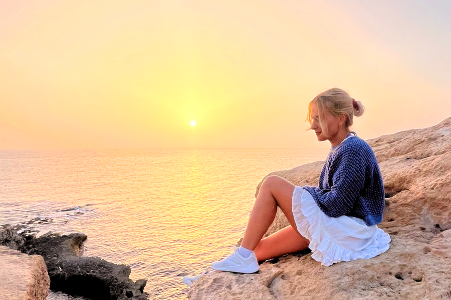 Una mujer sentada sobre unas rocas junto al mar, con el sol poniéndose detrás de ella, mostrando cómo la luz de la hora dorada crea fotos cálidas y preciosas.