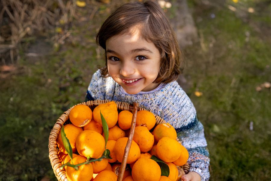Una niña de pie bajo un sol intenso sosteniendo un cuenco con naranjas, mostrando la dificultad de hacer fotos con el sol del mediodía.