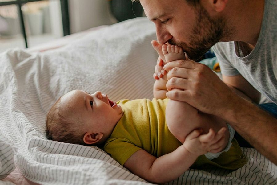 Un padre besa los pies de su bebé, como inspiración para una tarjeta del Día del Padre para un primer Día del Padre y mensajes Día del Padre llenos de cariño.