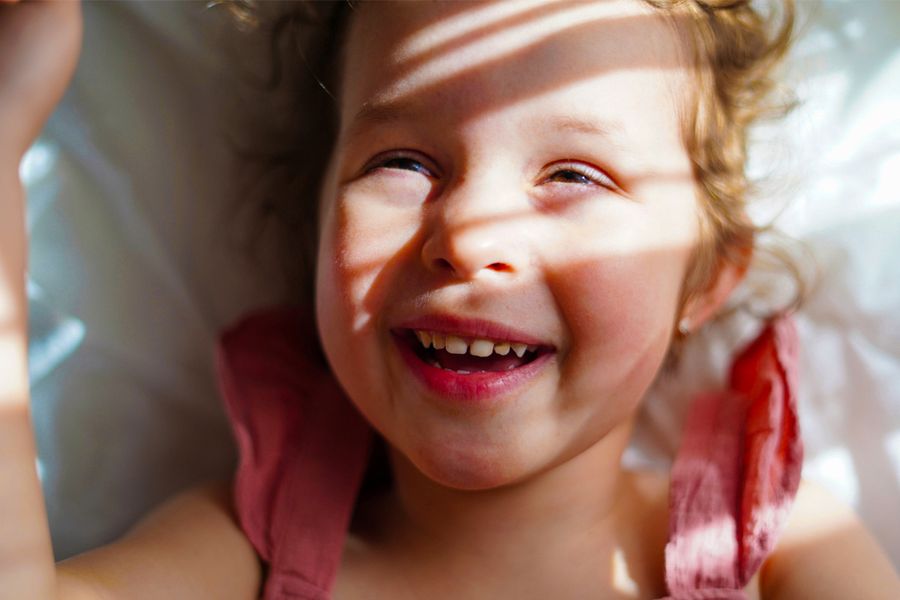 Una niña sonriente con sol y sombras suaves sobre el rostro, como inspiración para Hofmann y para aprender a hacer buenas fotos con mucho sol.