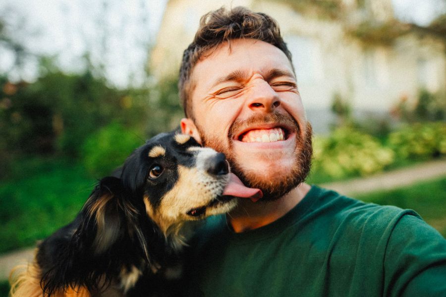 Un hombre sonríe junto a su perro, como inspiración para una tarjeta del Día del Padre desde el perro y mensajes Día del Padre con humor.