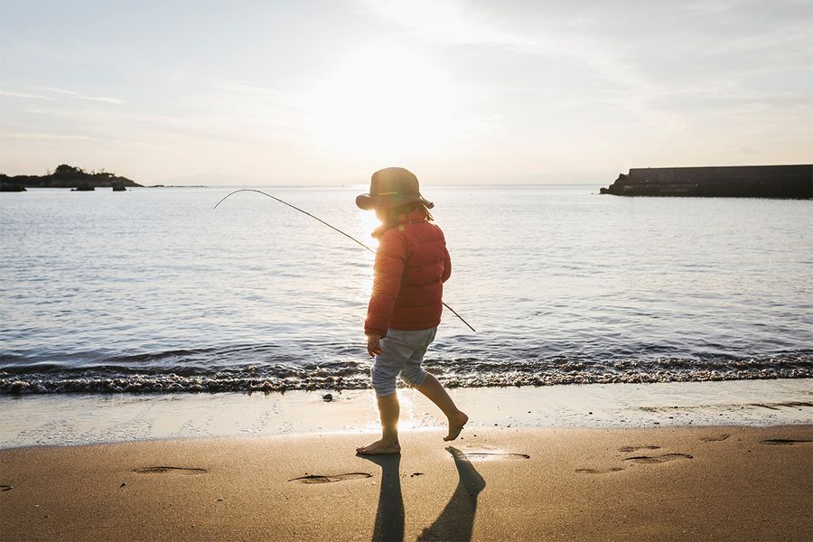 Un niño de pie en la playa junto al mar con una sombra marcada detrás, mostrando el efecto dramático de la fotografía de siluetas con luz solar.