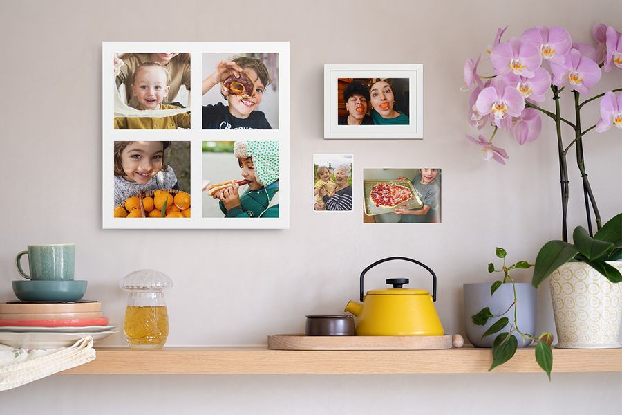 Una balda de madera con objetos decorativos del hogar se sitúa bajo un collage de fotos personalizado de niños, una foto impresa divertida enmarcada y dos fotos familiares en la pared, mostrando ideas para decorar con fotos impresas en la pared.