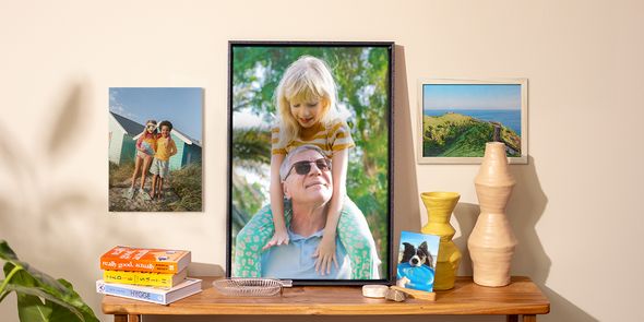 Una selección de fotos impresas de Hofmann colocadas por la casa, con una foto de un perro sobre una mesa auxiliar, un póster de niños en la pared y dos fotos enmarcadas, como inspiración para fotos en la pared y decoración primaveral del hogar.