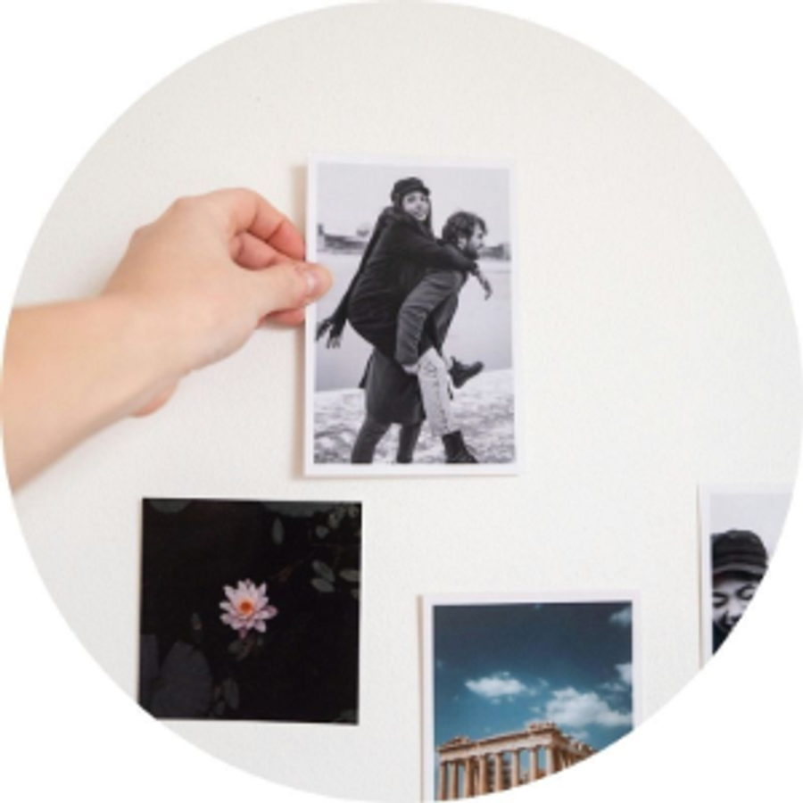 Una mano sostiene una foto impresa de una pareja junto a otras fotos impresas, ilustrando la historia de pedida de Andrea y una idea de pedida llena de recuerdos con Hofmann.