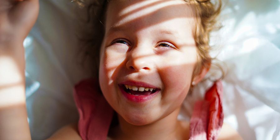 Una niña sonriente con sol y sombras suaves sobre el rostro, como inspiración para Hofmann y para aprender a hacer buenas fotos con mucho sol.