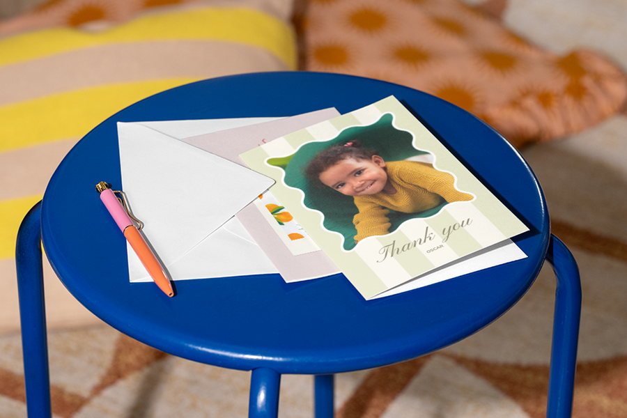 Una tarjeta para profesores personalizada de Hofmann con la foto de una niña en la portada está sobre un taburete con un bolígrafo al lado, como inspiración para frases para profesores de agradecimiento con un tono cercano y respetuoso.