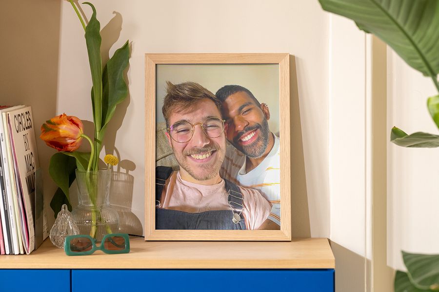 Una foto enmarcada de dos hombres haciéndose un selfi al sol está sobre un aparador junto a un jarrón, unas gafas de sol y una revista, como inspiración para decoracion salon verano y decoracion casa verano.