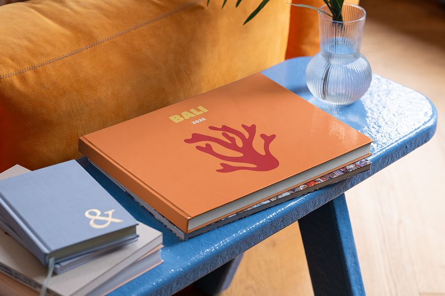 Un fotolibro de viaje horizontal personalizado de Hofmann sobre Bali está colocado sobre una mesa de centro azul, como inspiración para decoracion salon verano y los toques finales de decoracion casa verano.