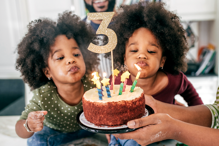 Dos niñas gemelas a punto de soplar las velas de su tarta de 3er cumpleaños, una inspiración perfecta para regalos de cumpleaños e ideas de regalo de cumpleaños de Hofmann.
