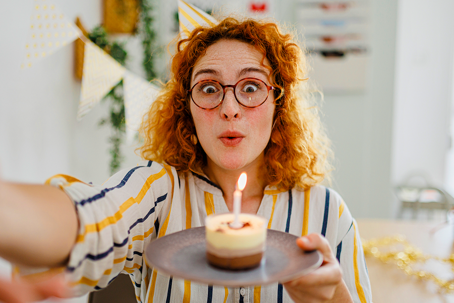 Una mujer de pelo rizado pelirrojo sostiene un cupcake con una vela, como inspiración para felicitaciones de cumpleaños para una compañera de trabajo y tarjetas de cumpleaños de Hofmann.
