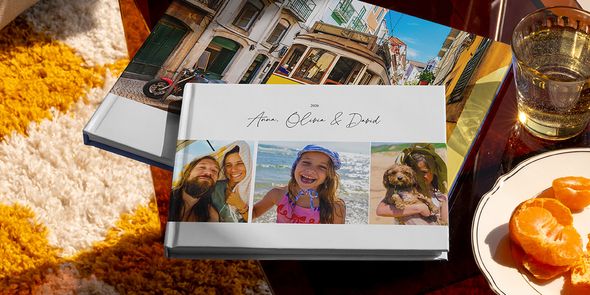 Se muestran juntos dos fotolibros de viaje de Hofmann, uno en formato horizontal con fotos familiares de viaje en la portada y otro con una imagen de un tranvía de vacaciones, como inspiración para distintos tipos de álbum de fotos de viaje personalizado.