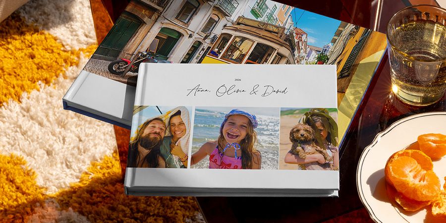 Se muestran juntos dos fotolibros de viaje de Hofmann, uno en formato horizontal con fotos familiares de viaje en la portada y otro con una imagen de un tranvía de vacaciones, como inspiración para distintos tipos de álbum de fotos de viaje personalizado.