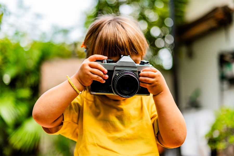 Una niña toma fotos con una cámara, reflejando las ideas de vacaciones en casa creativas de Hofmann.