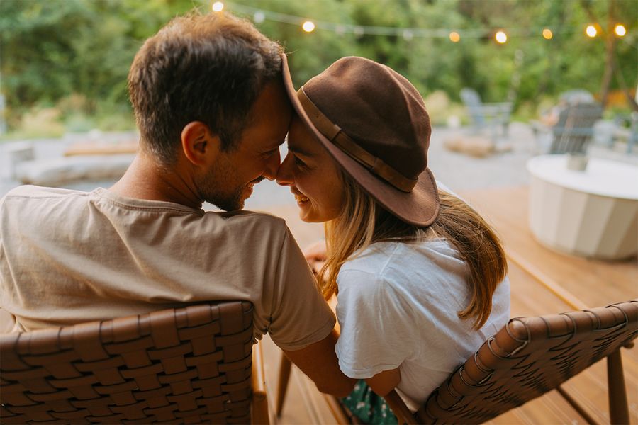 Un hombre y una mujer se abrazan cariñosamente sentados en un jardín decorado con luces, un momento romántico de las ideas de vacaciones en casa para parejas de Hofmann.