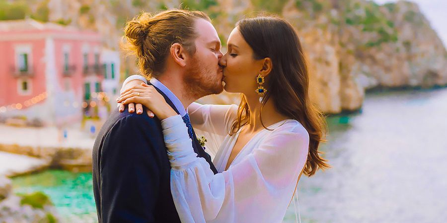 Una novia y un novio se besan el día de su boda con un fondo de estilo mediterráneo, reflejando las tendencias bodas 2026 y el estilo de boda personalizado de Hofmann.