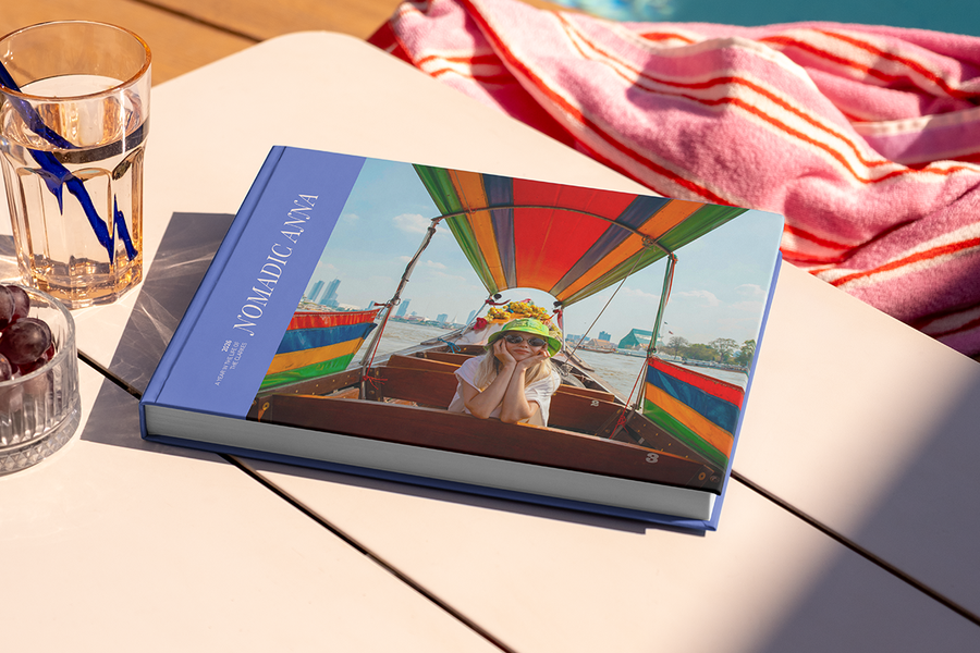 Un gran álbum de fotos de viaje en formato horizontal, titulado 'Nomadic Anna', está sobre una mesa, con la foto de una chica de viaje en la portada, ilustrando las ideas de título para álbumes de fotos de viajes de Hofmann.