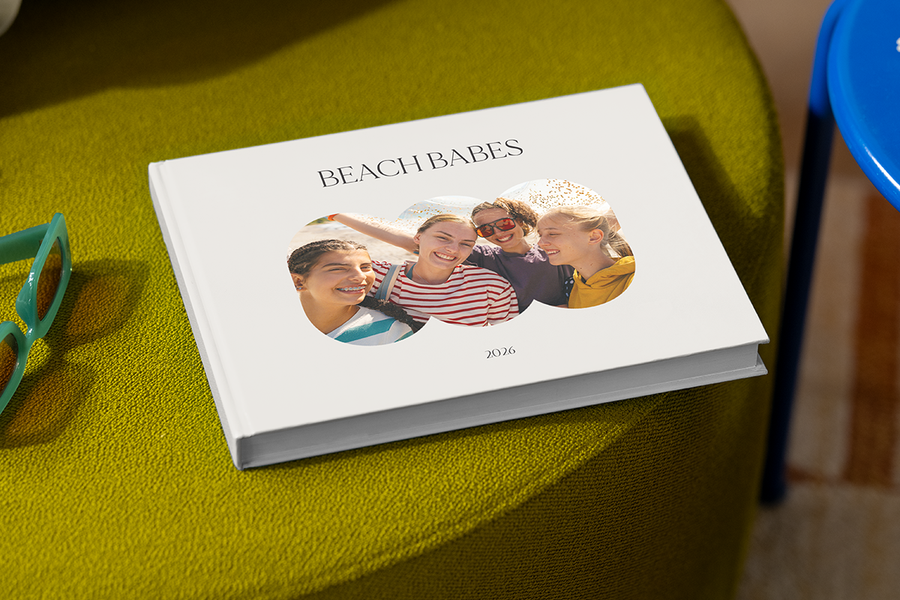 Un álbum de fotos con cuatro chicas sonriendo en la portada se titula 'Beach Babes', ilustrando las ideas de título para álbumes de fotos de viajes con amigas de Hofmann.