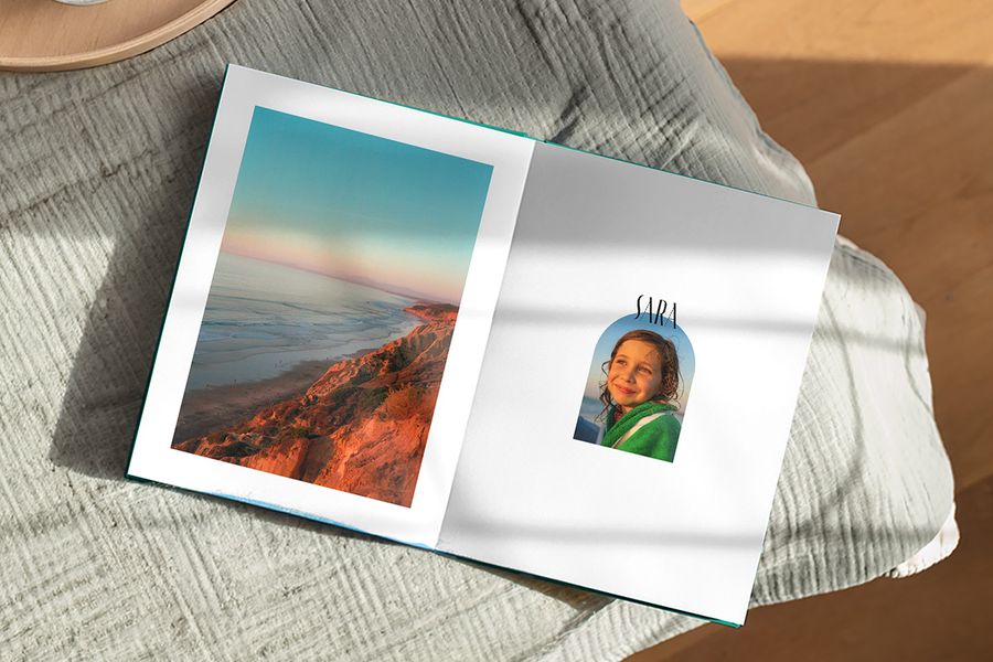Un álbum de fotos abierto muestra un precioso paisaje en una página y una foto de una chica con el pie de foto 'Sara' en la otra, ilustrando el diseño Artisan Masking de Hofmann con marcos divertidos inspirados en postales y sellos vintage.