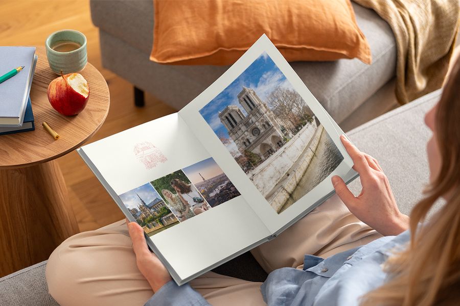 Una mujer sostiene en su regazo un álbum de fotos abierto con distintas fotos de viaje, ilustrando el diseño Graphic Getaways de Hofmann inspirado en carteles de viaje vintage y mapas ilustrados de ciudades.
