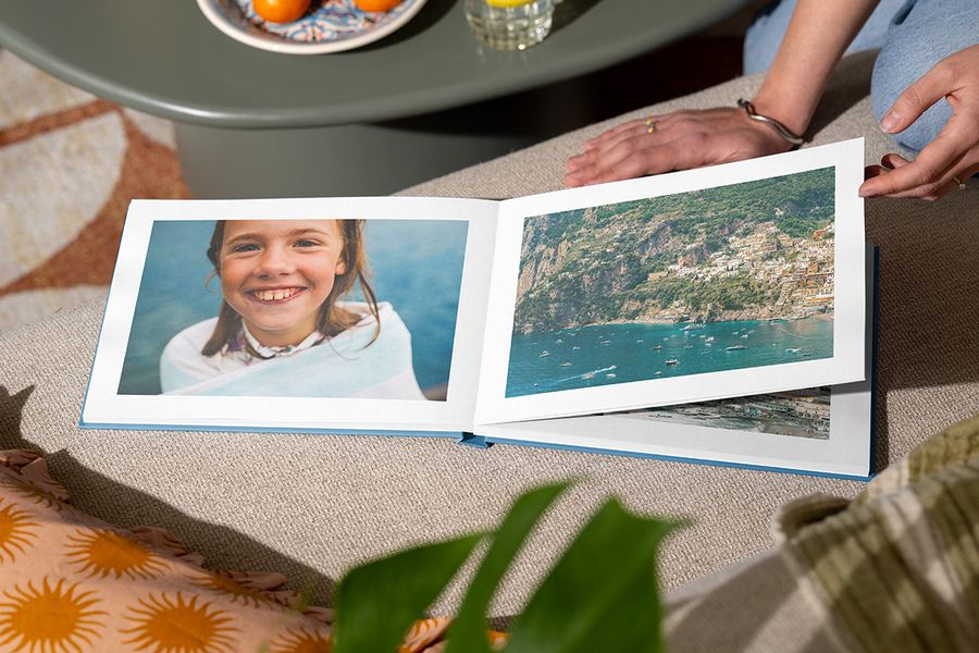 Un álbum de fotos abierto muestra a una chica sonriendo junto al mar en una página y una vista de playa en la otra, ilustrando el diseño Holiday Escape de Hofmann con fotografías inmersivas a página completa.
