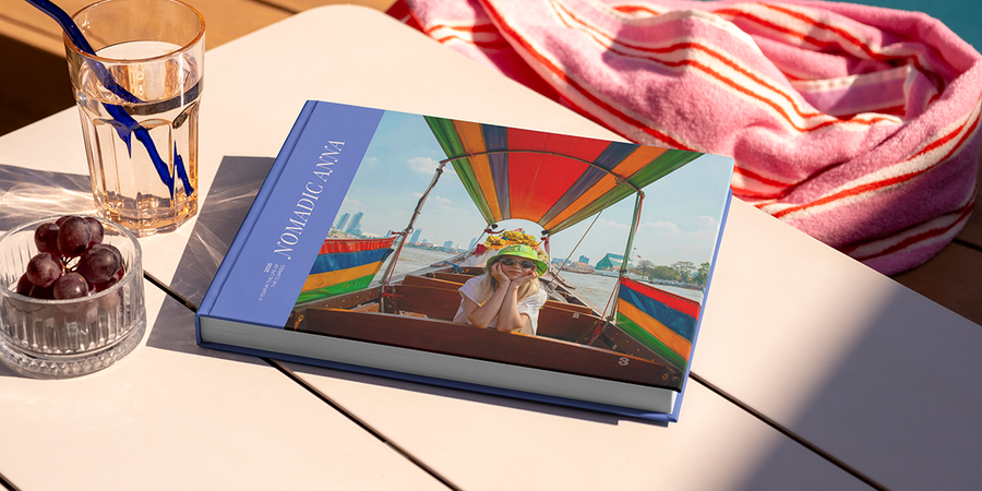 Un gran álbum de fotos de viaje en formato horizontal, titulado 'Nomadic Anna', está sobre una mesa, con la foto de una chica de viaje en la portada, ilustrando las ideas de título para álbumes de fotos de viajes de Hofmann.