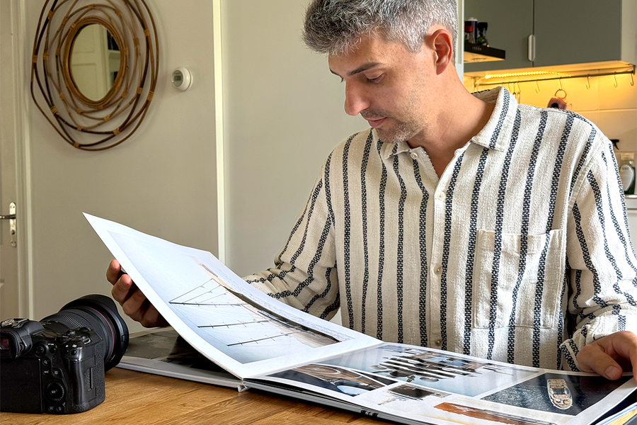 Charl van Rooy está sentado en su cocina mirando su portafolio abierto, con su cámara a su lado sobre la mesa, ilustrando la guía de Hofmann para crear un portafolio de fotografía en formato álbum de fotos.