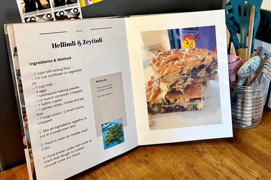 Un libro de recetas personalizado abierto se encuentra en una cocina, con un tarro de cucharas y utensilios de cocina de fondo, ilustrando los consejos de Hofmann para elegir qué recetas incluir antes de crear tu propio libro de recetas.